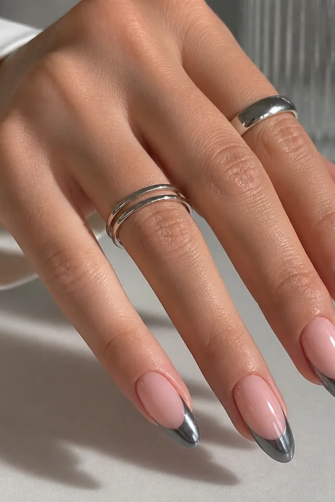 Almond nails with a cool rosy pink base. The French tips are gunmetal chrome - a darker smoky silver that still reflects light. The smile line is clean and slightly wider than a micro-arc, with a matte-to-mirror contrast from the chrome sheen.