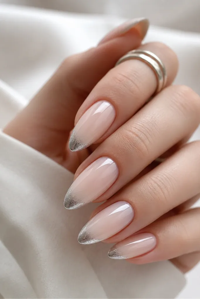 Almond nails with a milky nude base. The French tip fades from strong mirror silver at the very edge into a softer, almost clear shimmer toward the center of the tip. The fade is smooth with no harsh line.