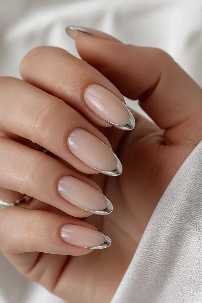 Almond nails with a nude base. The French tip is silver chrome in the center, but the sides near the sidewalls stay clear and nude, making a clean channel effect. The chrome edge is crisp and separated from the side areas.