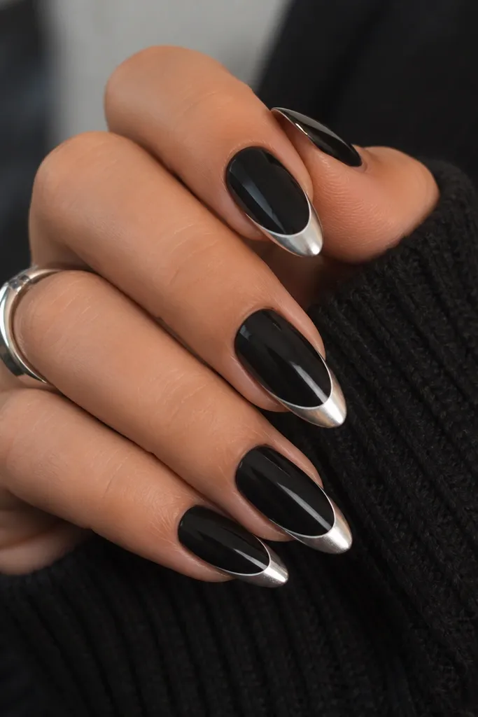 Medium length almond nails. A black base covers the nail. A slim white French outline hugs the smile line, and the tip is coated in silver chrome with a crisp, high-contrast edge.