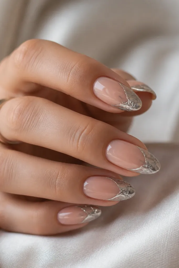Almond nails with a nude base. The tips have a white marble pattern, and over the marble, there is a silver chrome layer that makes the veins look metallic.