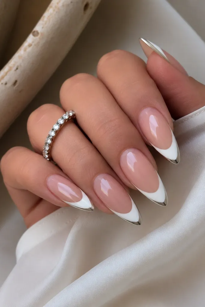 Long almond nails with icy white French tips. Only the very outer edge of each tip has mirror chrome, leaving most of the white matte-glossy and clean.