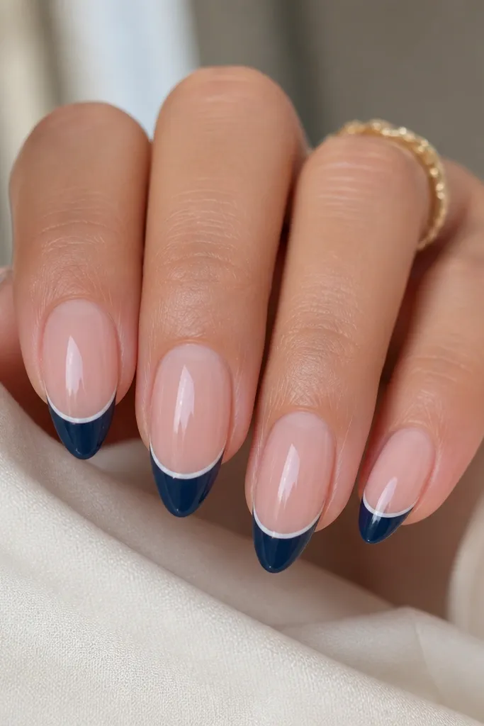 Medium almond nails with a glossy sheer nude base. The French tip is navy, but there's a razor-thin white line separating the navy from the nude, running exactly along the smile curve. The edges look sharp, like vinyl.