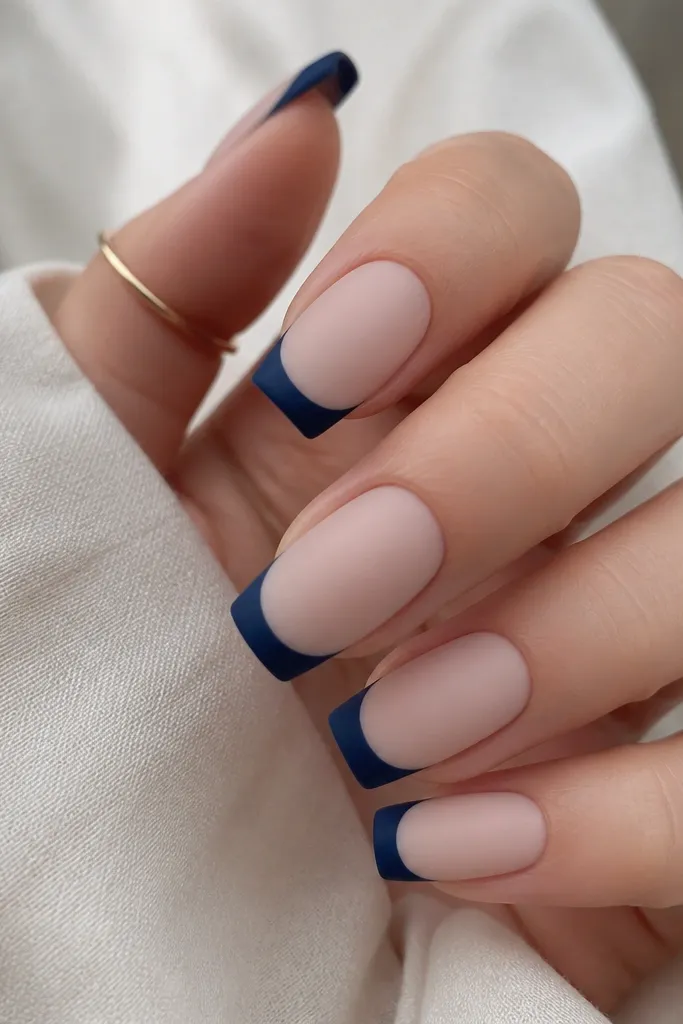 Long squoval nails with a milky nude base that's matte. The French tips are navy with a matte finish too, and the smile line is clean and slightly wider than micro French. No shine except the nail silhouette.