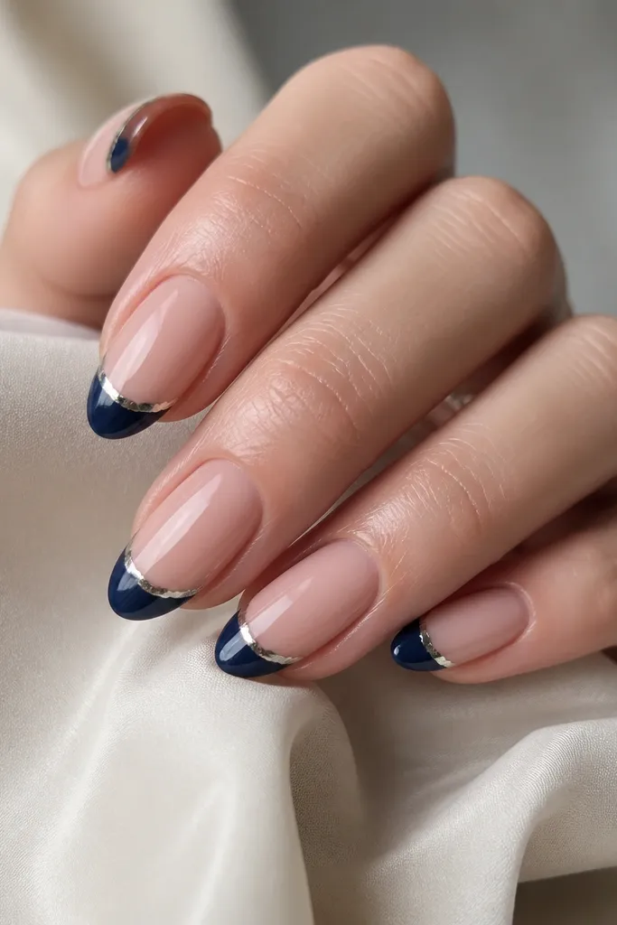 Medium almond nails in glossy sheer pink. The French tips are navy and there's a narrow strip of metallic silver foil right at the smile line, like a tiny crown. The foil has slight natural wrinkles but stays centered and straight.