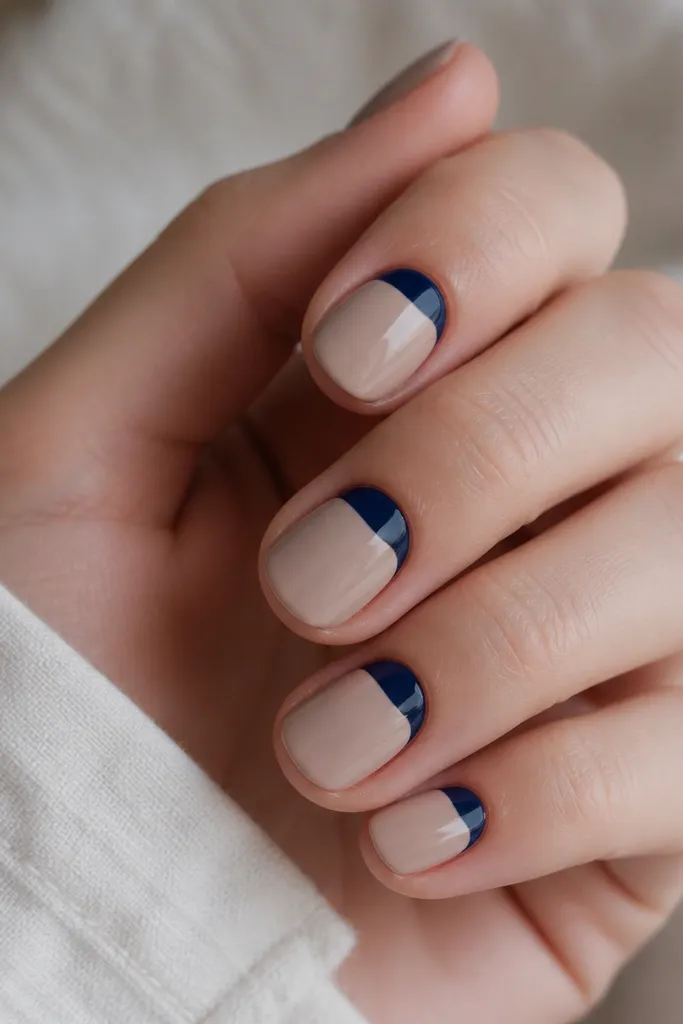 Short round nails with a glossy nude base. Instead of a traditional tip, the navy sits at the cuticle area as crisp half-moons. The rest of the nail is nude gloss with a clean boundary line around the half-moon.
