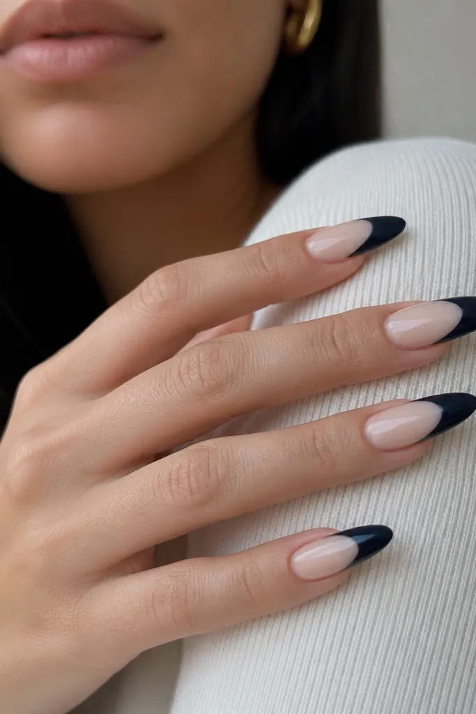 Long almond nails. The base is sheer nude. The navy French tip is painted as a C-shape leaving a small negative-space window near the smile line, creating a cutout effect. The negative area is crisp and matches the curve.