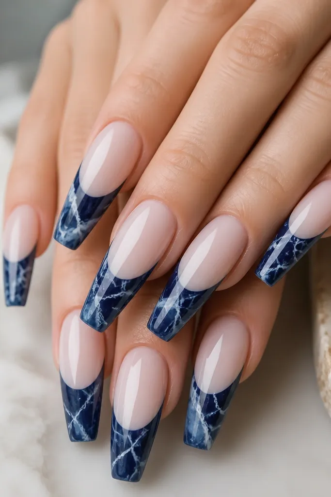 Long coffin nails with a glossy milky nude base. The French tips are navy marble with thin white vein lines that branch like marble. The navy is swirled, but the smile curve is still clean and defined.