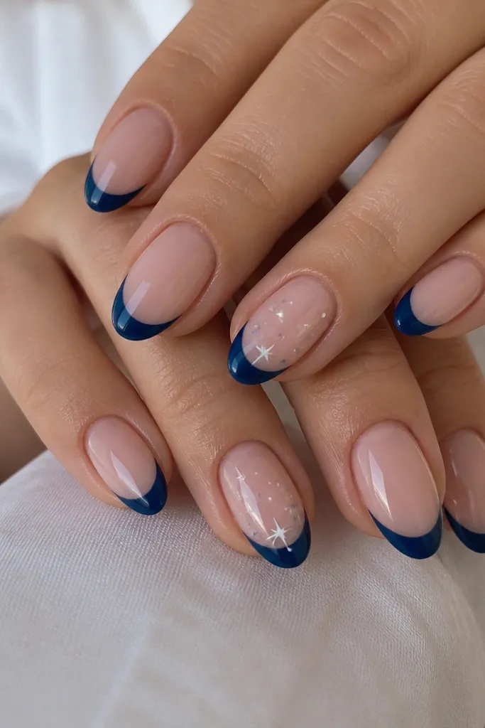 Medium almond nails. Glossy sheer nude base. Navy French tips in glossy finish, and on two nails there are tiny matte dot stars in white and light gray scattered near the smile line like small constellations.