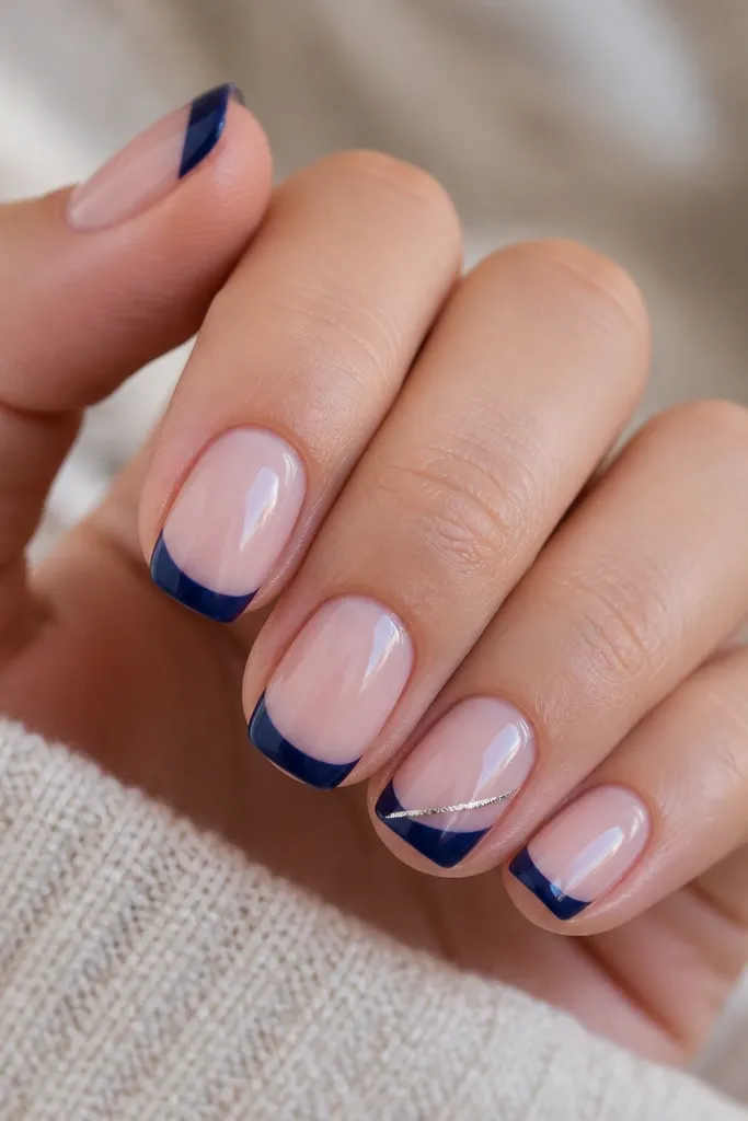 Short squoval nails with a glossy nude base. The French tip is navy with a clean smile line. One nail has a thin diagonal accent line in silver running from mid-tip down toward the side, staying inside the navy area.