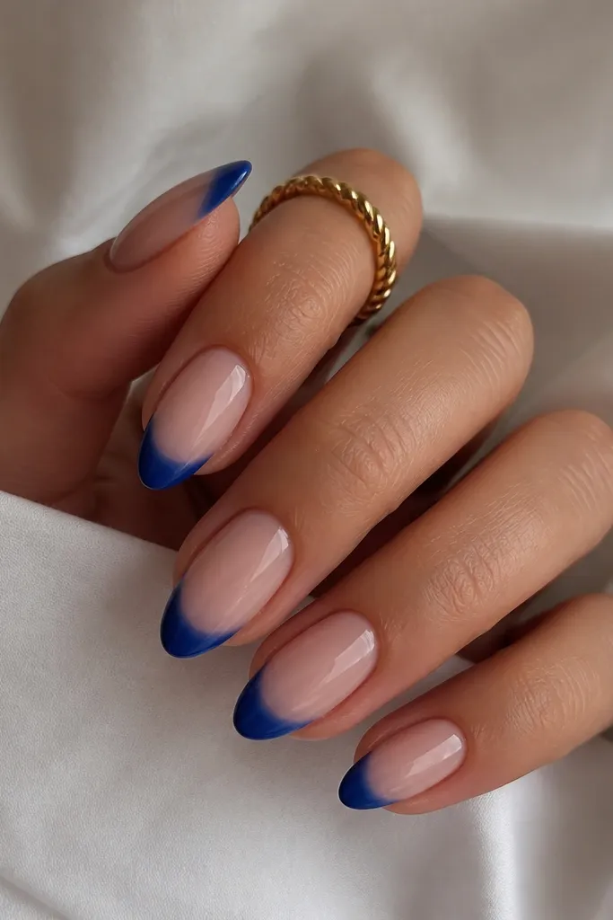 Medium almond nails. Base is glossy nude. The French tip has an ombre gradient that starts with a slightly lighter royal blue near the smile line and fades to darker navy at the very edge. The gradient is smooth, no harsh lines.
