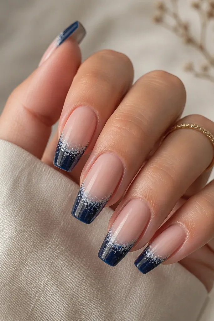 Medium coffin nails. Glossy sheer nude base. Navy French tips with a solid navy fill. Over the navy, there are tiny white speckles and short streaks like marble dust, concentrated near the smile line and fading outward.