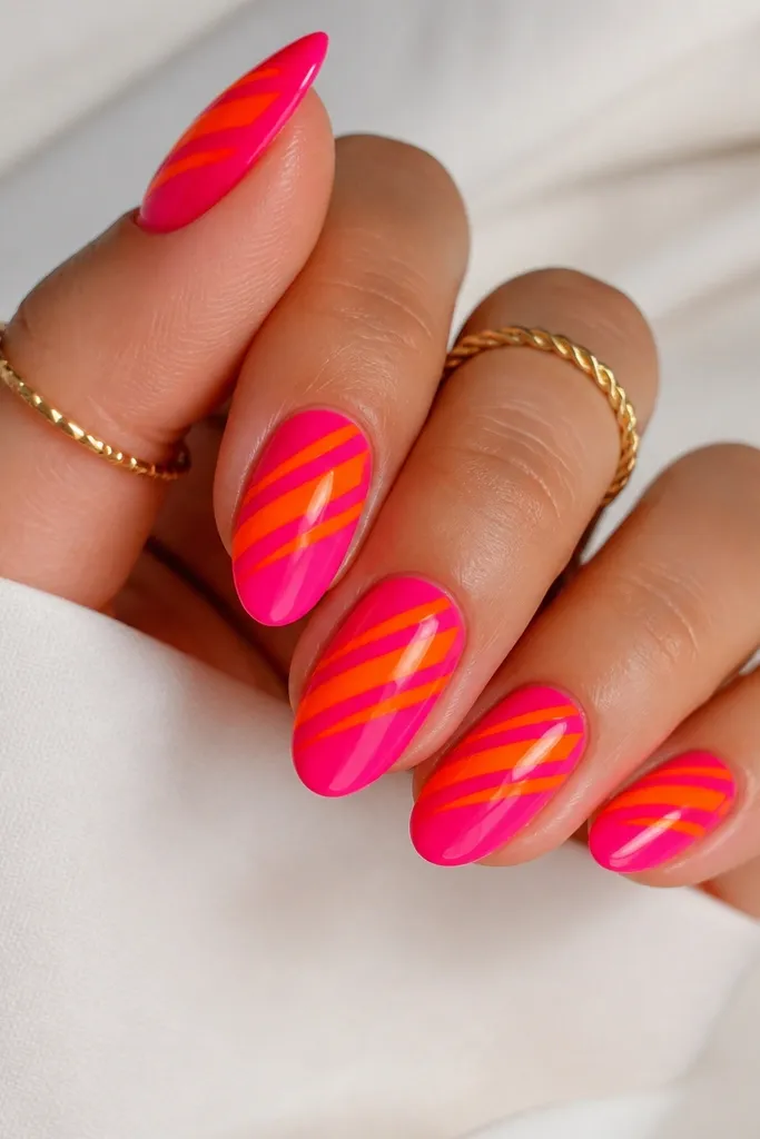 A glossy hot pink base with diagonal neon orange slashes across the center of each nail. The slashes are separated by thin negative space lines, so the pink shows through between orange strokes.