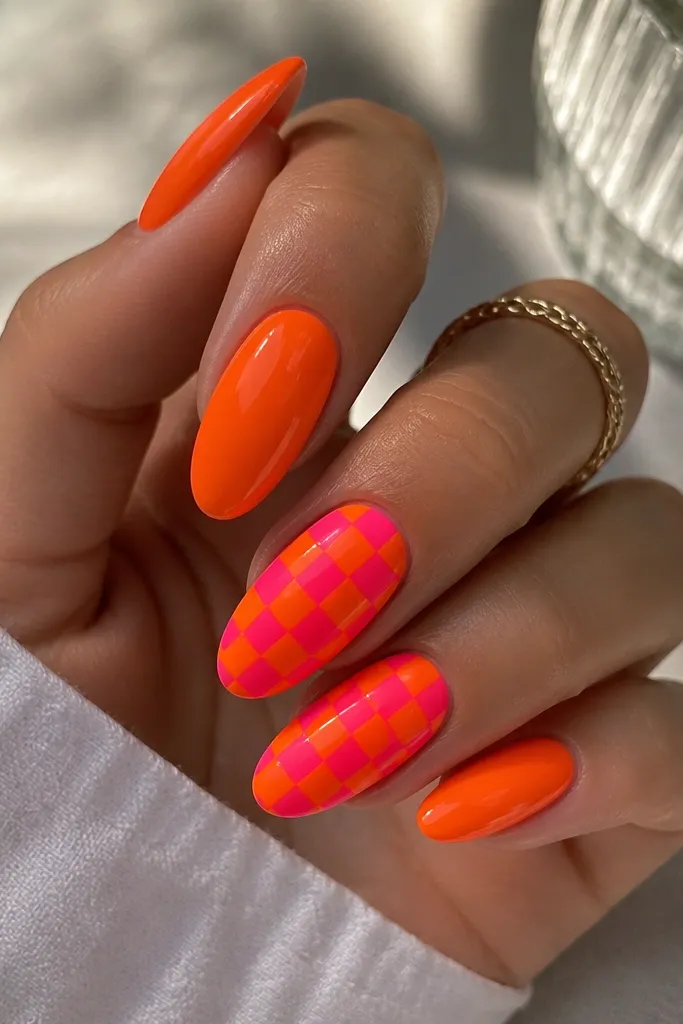 Three nails are solid neon orange with glossy shine. Two accent nails are a checker pattern of hot pink and neon orange squares, with crisp straight edges and consistent square size.