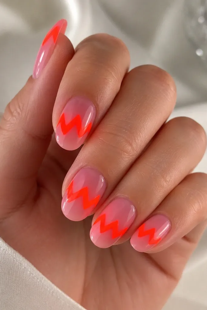 Pink jelly nails with a bold neon orange zigzag band across the center. The zigzag has sharp corners and clean edges, and the jelly base looks slightly translucent.