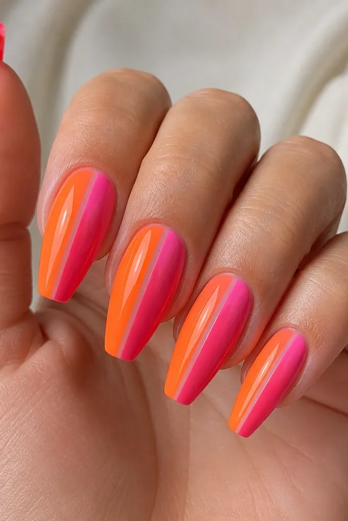Coffin nails with a diagonal split. The left side is orange, the right side is hot pink. A thin clear negative-space stripe runs down the center. Glossy top coat with sharp diagonal edges.