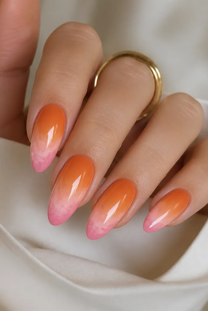 Almond nails. The base fades from deeper orange near the cuticle to lighter orange near the middle. The tip has a soft pink cloud effect that looks airbrushed, with a smooth transition. Glossy finish.