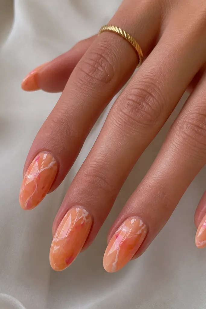 Medium almond nails. Orange marble base with thin white lines. Small pink accents appear as dots and tiny streaks near the center. Glossy, marble effect is subtle.