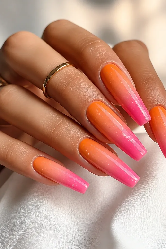 Coffin nails with ombre from orange at the cuticle to pink at the tip. Tiny white sparkles are sprinkled near the pink area. Glossy and smooth gradient.