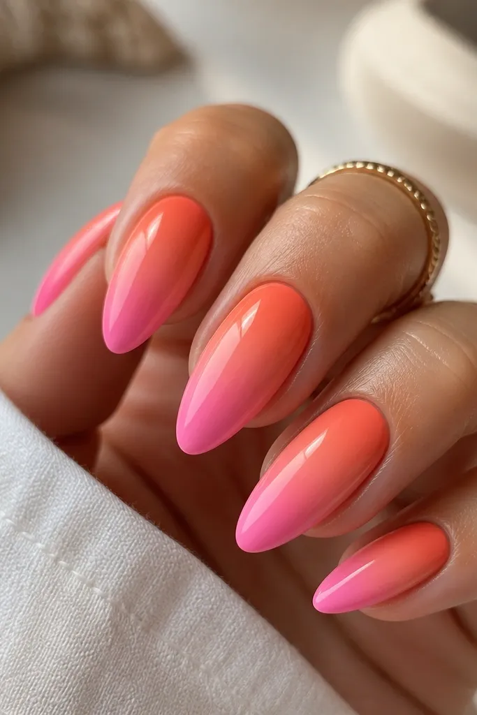 A set of almond nails with a smooth gradient: coral-orange at the cuticle blending into a bright bubblegum pink at the tip. The nails are glossy, with no extra art. The blend is narrowest near the cuticle and slightly wider toward the middle.