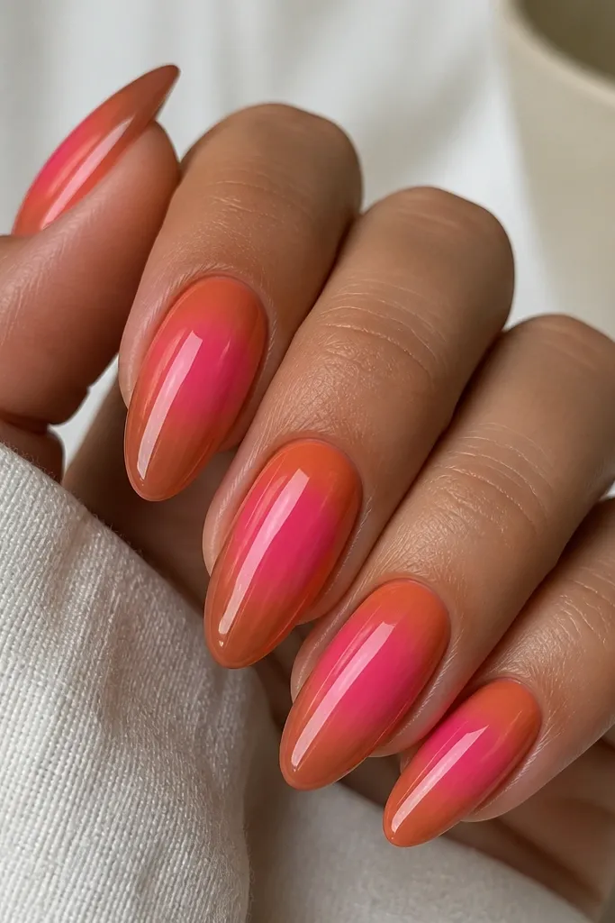 Almond nails with glossy finish. The center halo is bright pink, surrounded by a smoky orange fade toward the sides and tips. The outer edge is softer and slightly darker, but no sharp lines.