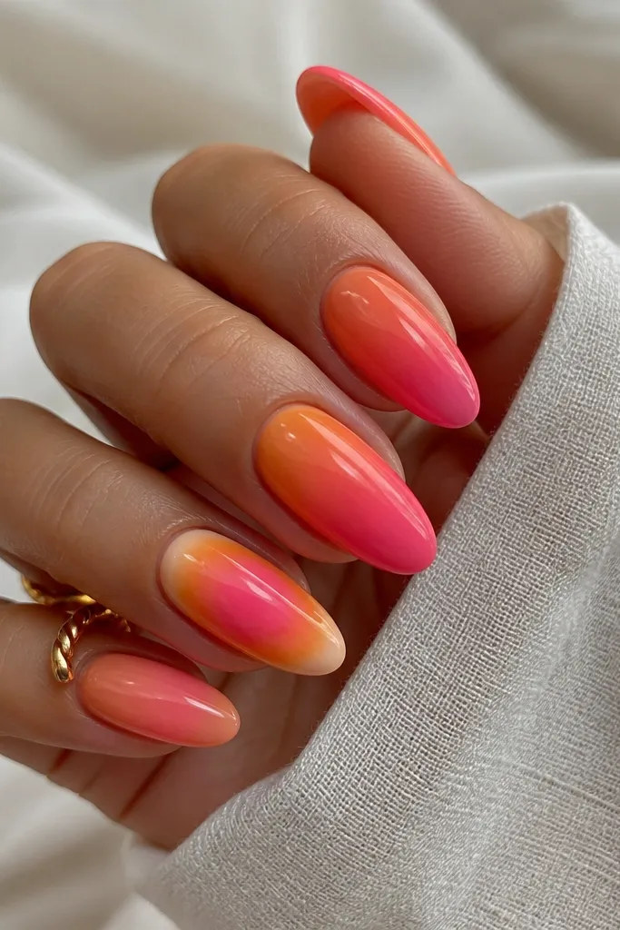 A full set where four nails are orange-to-pink ombre and one nail is aura. The accent nail has a pink center halo with orange smoke around it, on an almond shape. All nails are glossy and match in color family.