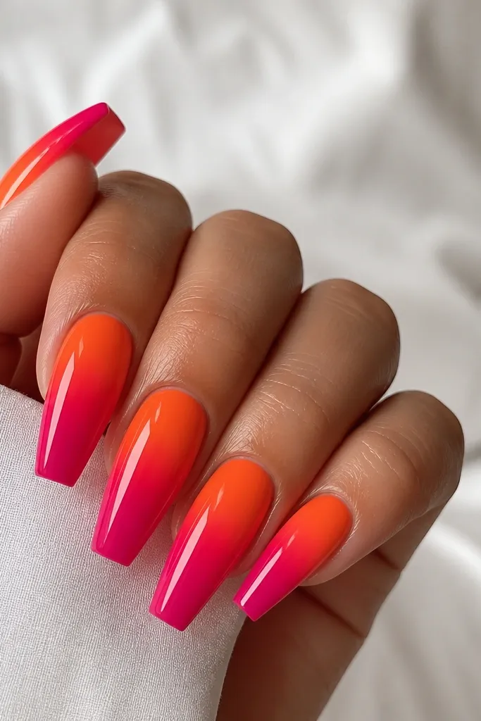 Coffin nails with a strong gradient. Tangerine orange sits at the cuticle, blending into vivid fuchsia at the tips. The blend is smooth but more dramatic than pastel sets. Glossy finish.