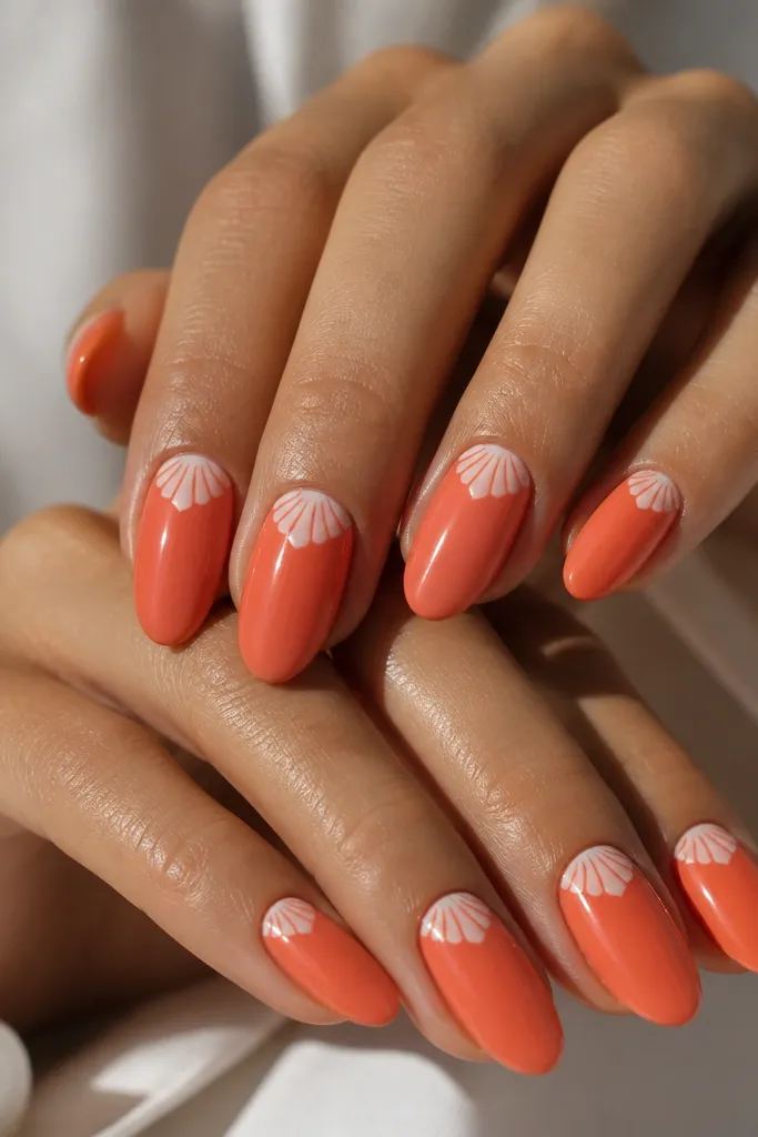 Medium almond nails in coral-orange. A white shell pattern sits along the side near the cuticle, shaped like a half-moon with curved ridges. Glossy finish, no glitter.