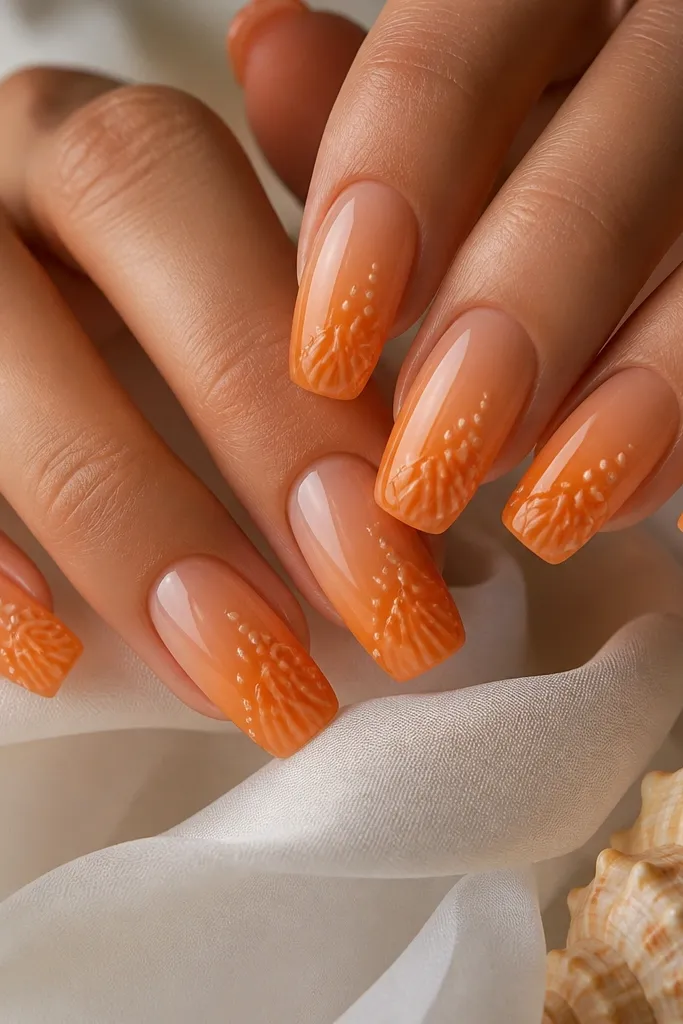 Long squoval nails with orange ombré fading from peach near the cuticle to deeper orange at the tips. Tiny pale cream dots and little curved ridges appear near the tip like mini shells. Glossy topcoat.