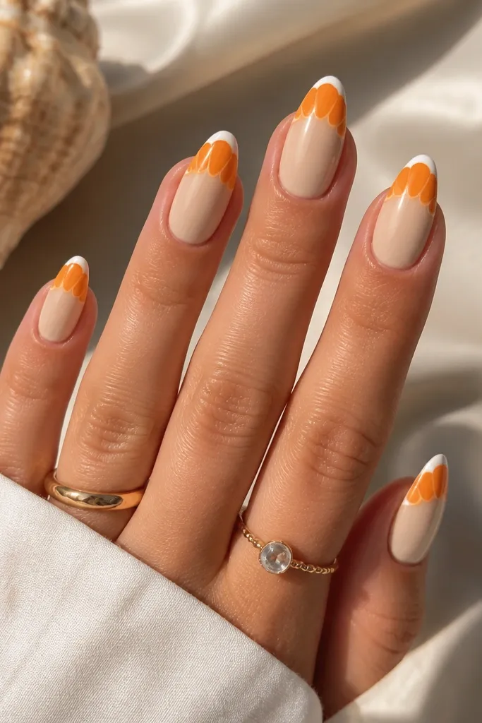 Medium almond nails with a sand beige base. The tips have bright orange shell ridges stacked like scallops, with a thin white outer curve. Glossy finish.