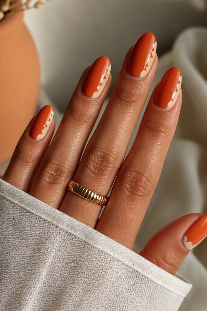 Medium almond nails in terracotta orange. At the side near the tip are cream scallop half-moons stacked like shell edges, with a glossy shine.