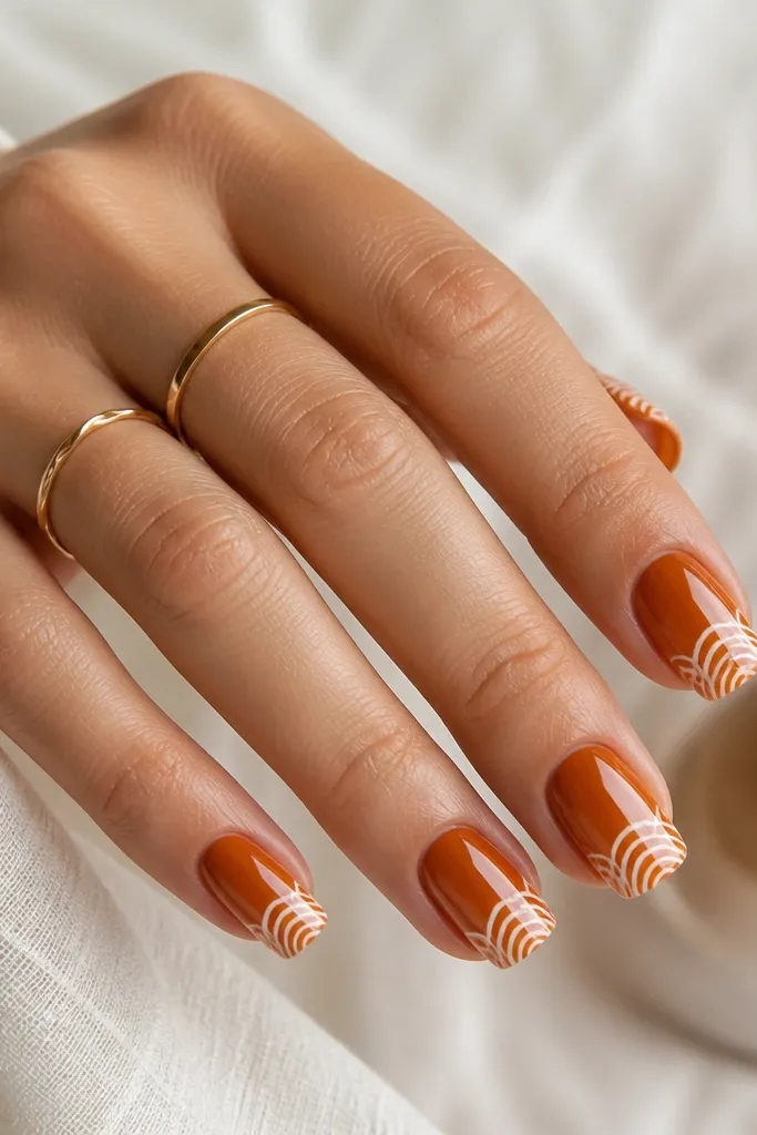 Medium square nails in burnt orange. Near the tip, white curved chevron shapes create a shell-like pattern. Glossy finish, no gems.