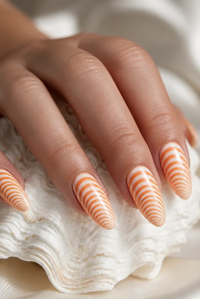Long almond nails with alternating orange and white curved stripes that fade in thickness toward the tip. The stripes look like shell ridges. Glossy topcoat.