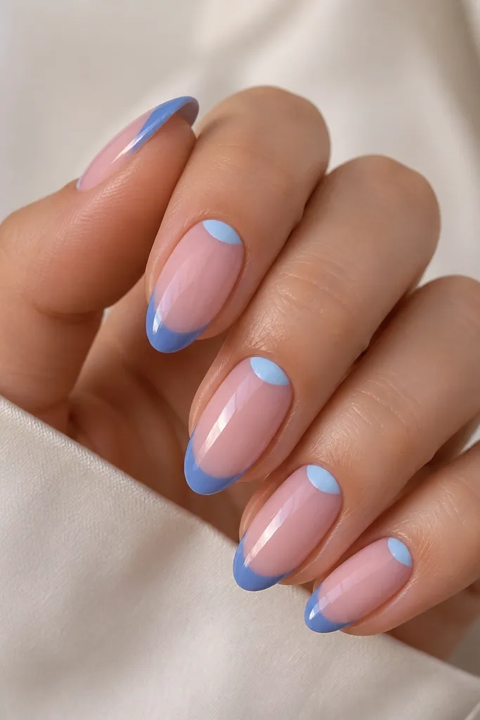 Medium-length almond nails with a blush pink base. The French tip is cornflower blue, and there's a smaller reverse half-moon in lighter blue near the cuticle, glossy.