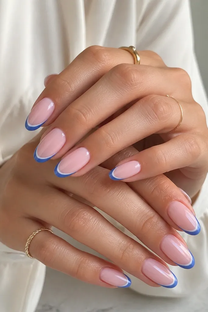 Medium almond nails with a baby pink base. The French tip is outlined in royal blue with a thin inner line, leaving the center of the tip lightly filled, glossy.