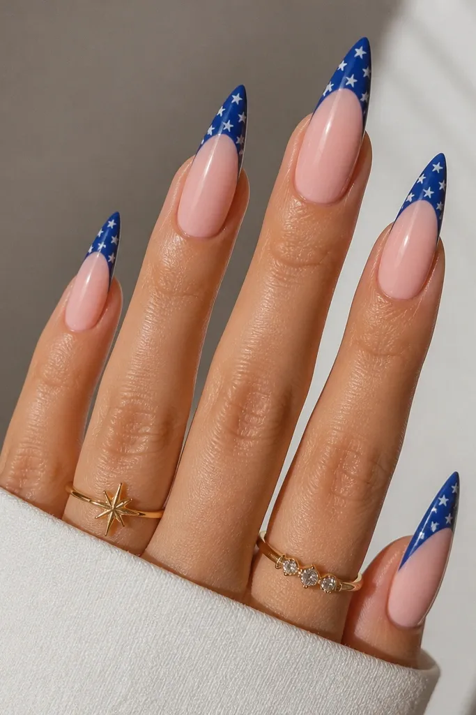 Long stiletto nails with creamy pink base. Solid blue French tips have tiny white star-shaped dots scattered near the tip edge, glossy.