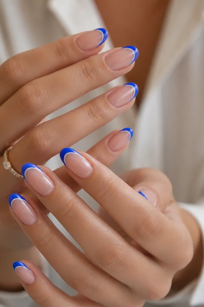 Medium almond nails with nude pink base. Electric blue French tips are edged with a thin white line just inside the tip border, glossy.