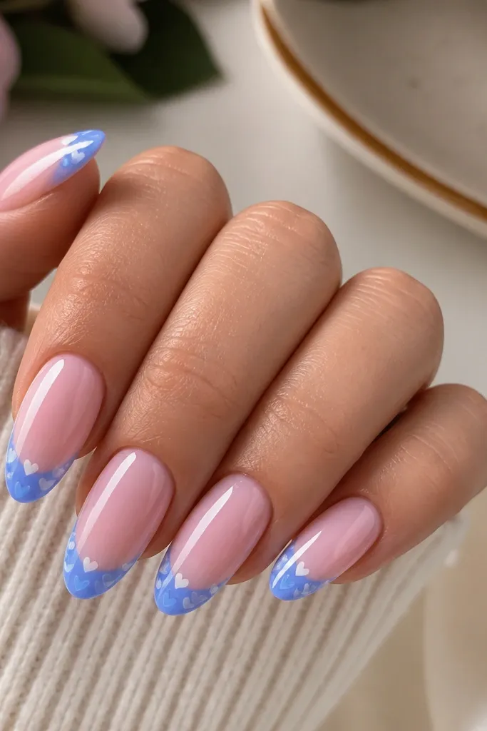 Long almond nails with pastel pink base. Blue French tips have tiny micro heart icons in a lighter blue and white near the tip edge, glossy.