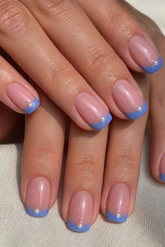 Medium squoval nails with dusty dusty pink base. Cornflower blue French tips include one small pearl stud per nail near the center of the tip edge, glossy.