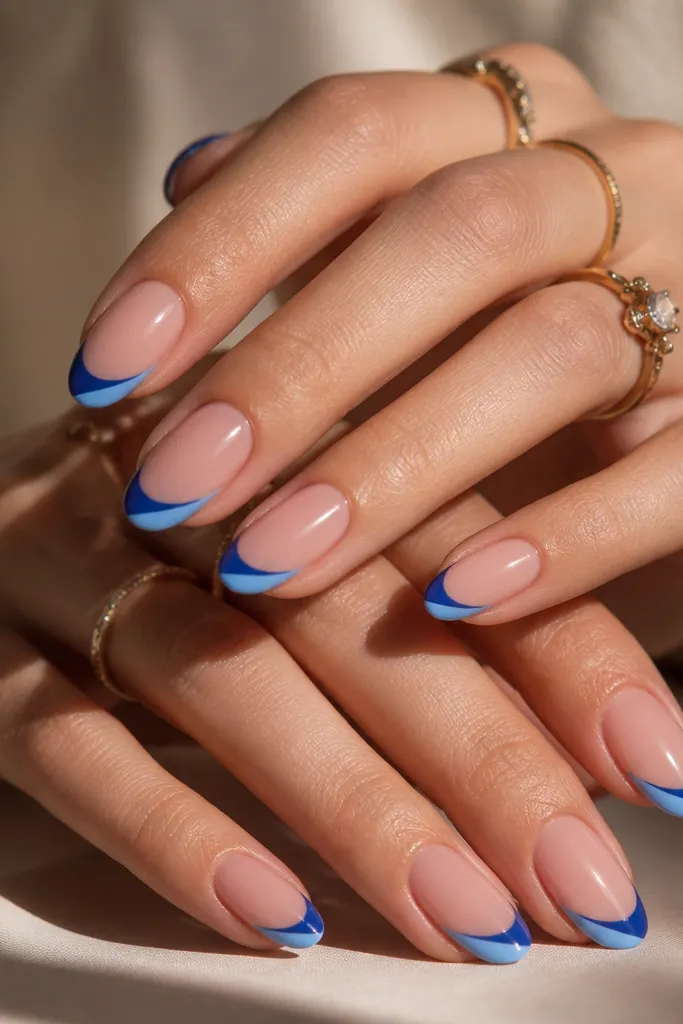 Medium almond nails with nude rosy base. Blue French tips include a diagonal half-stripe in lighter blue across the tip, glossy.