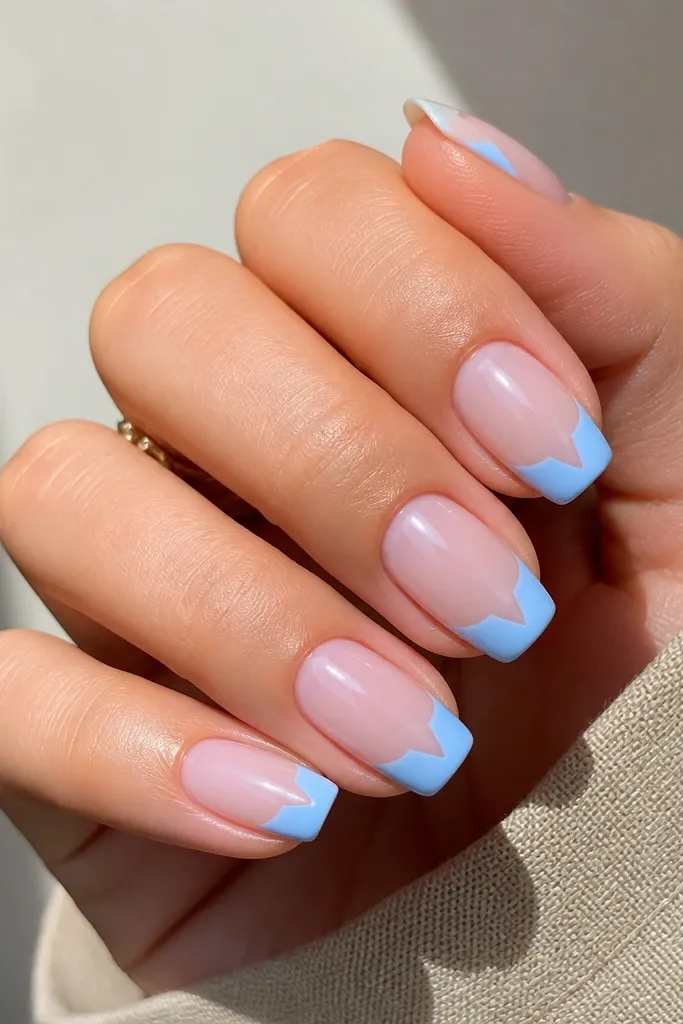 Medium squoval nails with pink base. Blue French tips leave a small negative-space triangle in the center near the smile line, glossy.