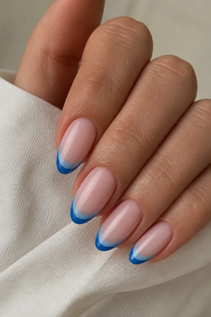 Short almond nails with milky pink base. The blue French tips have a two-layer look: darker blue at the very tip edge fading into lighter blue toward the smile line, glossy.