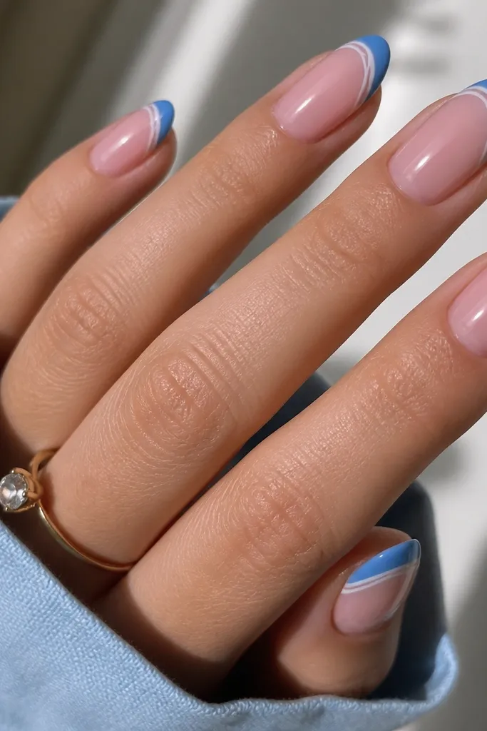 Medium oval nails with rose quartz pink base. Blue French tips include very thin white linework curves near the smile line, glossy.