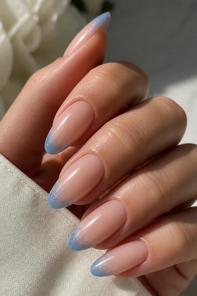 Long oval nails with soft nude pink base. Blue French tips fade into a micro glitter dust at the extreme tip edge, glossy.