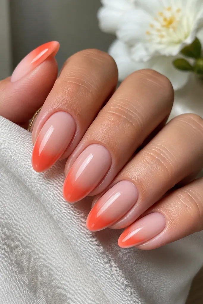 Set of medium almond acrylic nails. The base is soft milky pink. The tips fade from tangerine orange into coral, with a smooth French-style curve. High-gloss finish, no glitter.