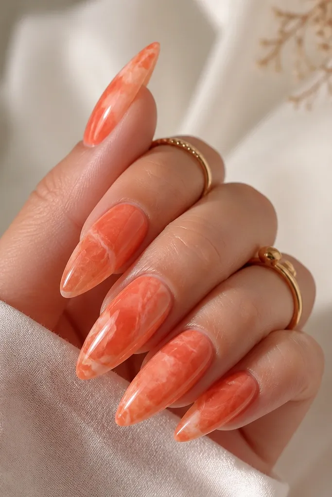 Long almond nails. Base is tangerine orange with a semi-sheer finish. Thin white-pink marble veins swirl through the orange, with a few soft coral streaks. Glossy top coat.
