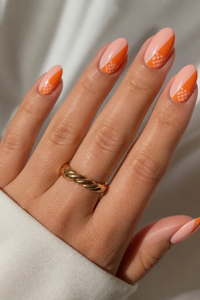 Medium almond nails. Each nail has a diagonal split: one half is milky pink, the other half is tangerine orange. On the orange half, a tiny checker pattern appears in a small triangle near the tip. Glossy finish.
