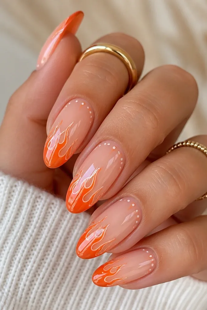 Medium almond acrylic nails with a peach-pink opaque base. The tips fade into bright tangerine flames that look hand-painted, with thin white "spark" lines at the flame edges and a few tiny orange dots near the cuticle. High-gloss top coat reflects light like a smooth glass layer.
