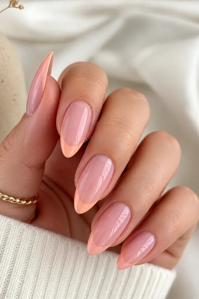 Almond nails featuring a thin peach French tip arcing across the edge, with a soft pink "skirt" that fades upward from the tip; high-gloss shine and crisp smile line.