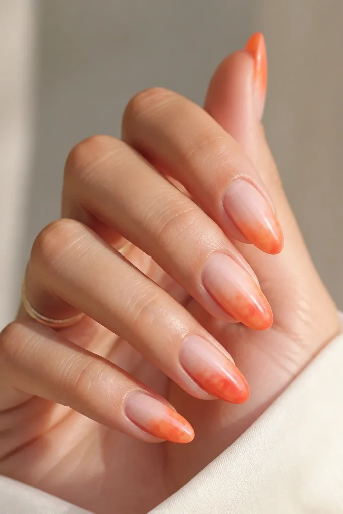 Almond nails with a sheer pink base and a watercolor-style tangerine orange fade concentrated at the tips; edges look soft and slightly speckled from blending.
